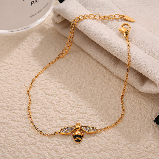 Gold bracelet with bee charm on a beige fabric background